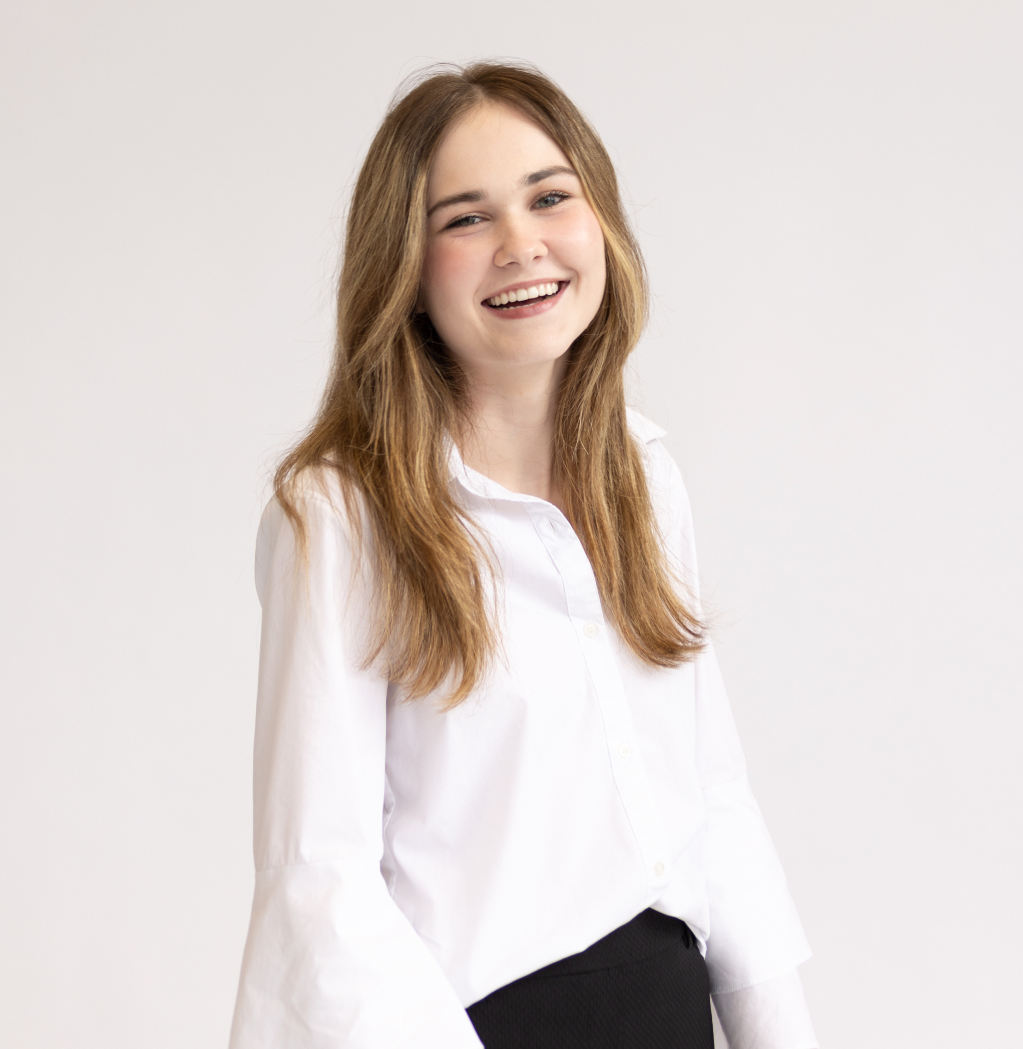 headshot of Kenzie, standing in a white button up top with black dress pants with. Laughing and smiling face while looking at the camera.